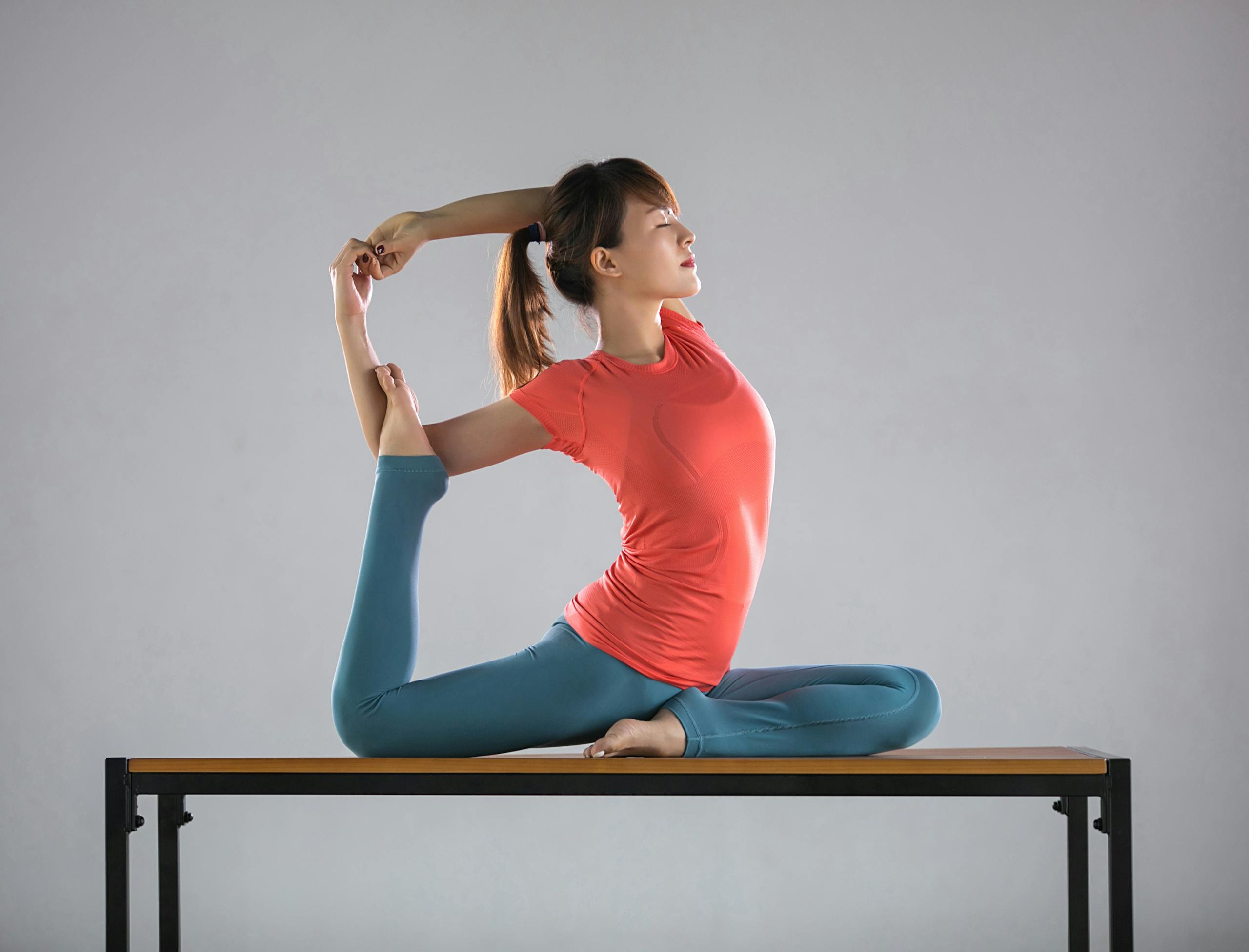 A woman demonstrates an advanced yoga pose on a table indoors, showcasing flexibility and balance.