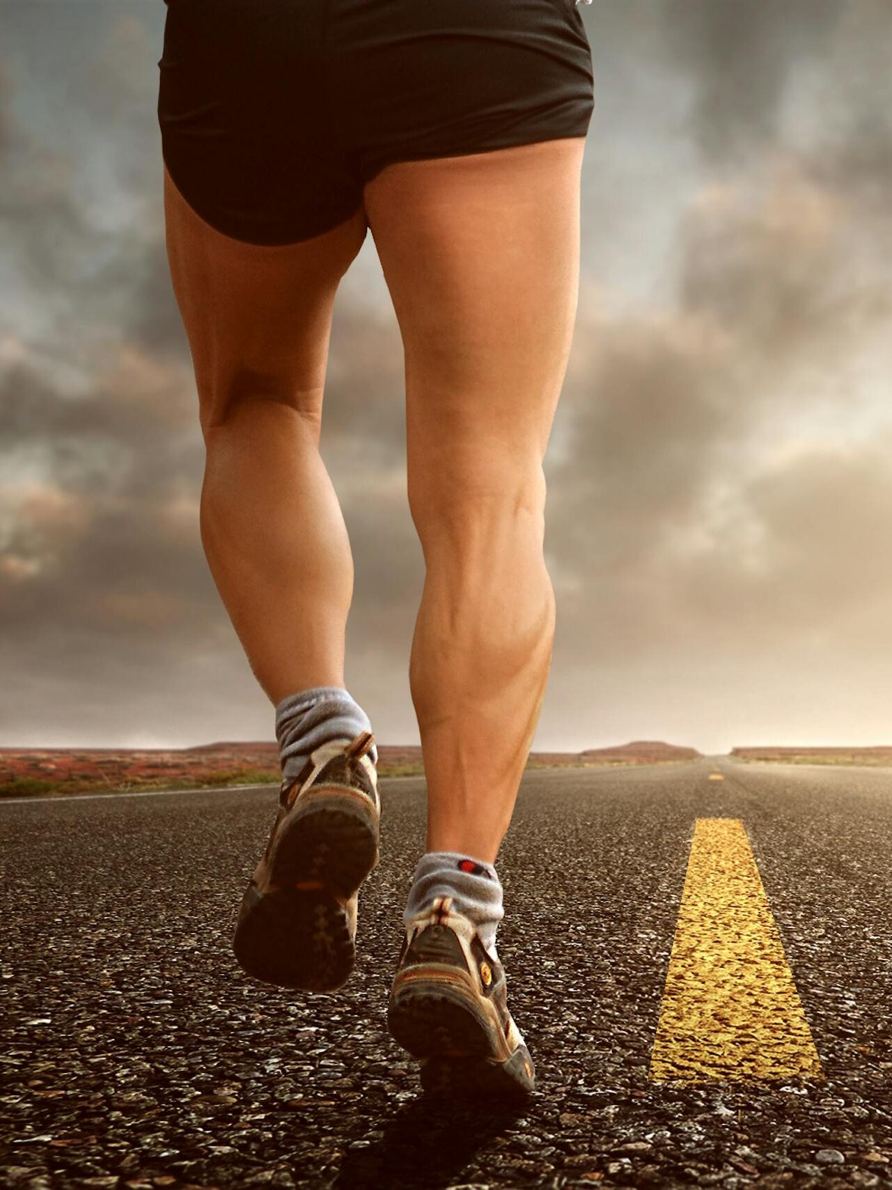 Runner's legs on a road during a sunset, symbolizing endurance and outdoor fitness training.