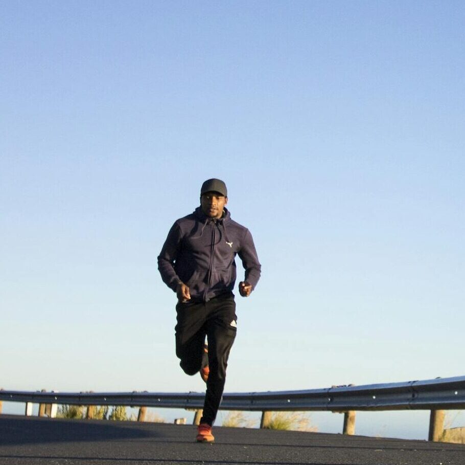 An athletic man jogging on an open road with a clear blue sky in Cape Town, South Africa.
