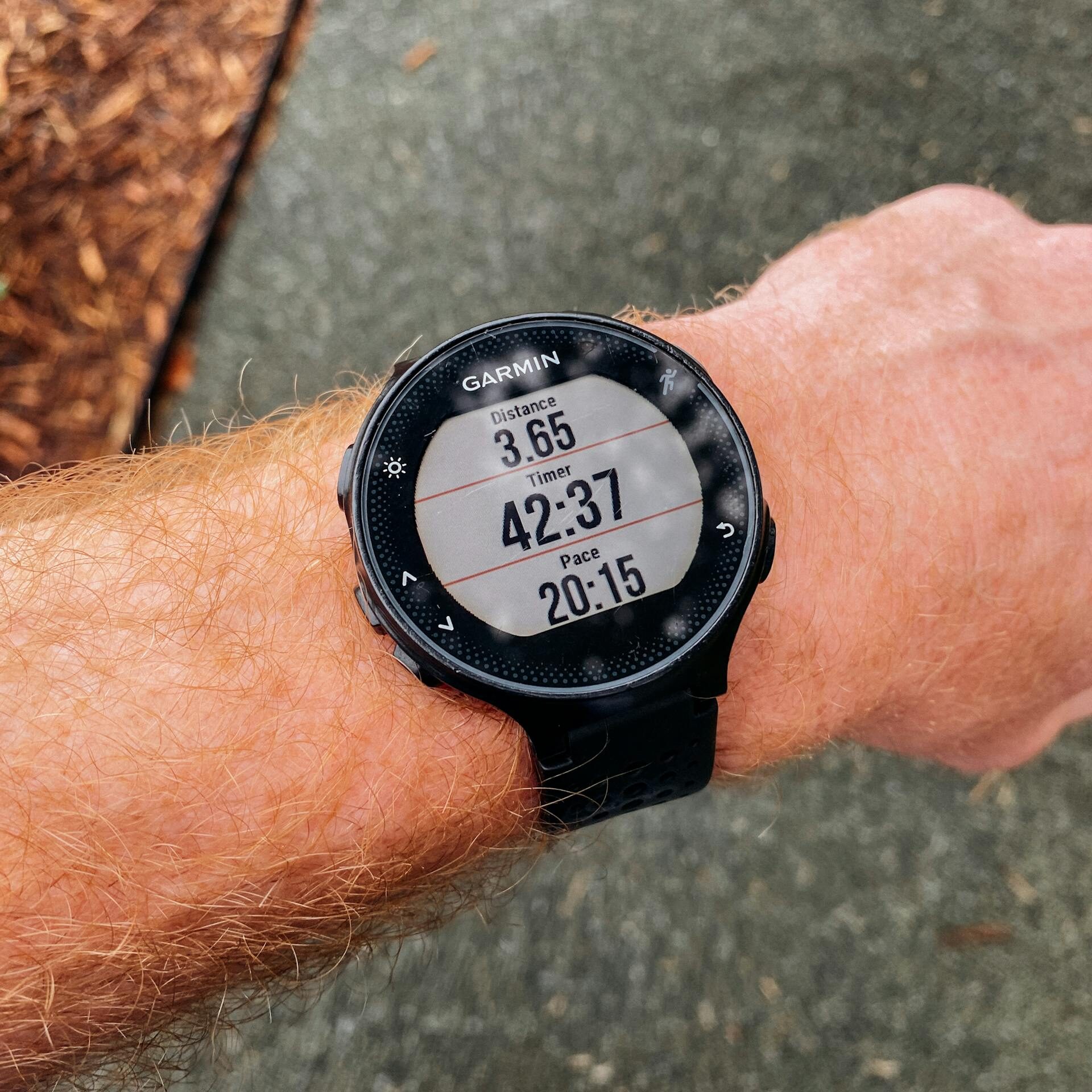 Close-up of a smartwatch showing running distance, time, and pace on a wrist outdoors.