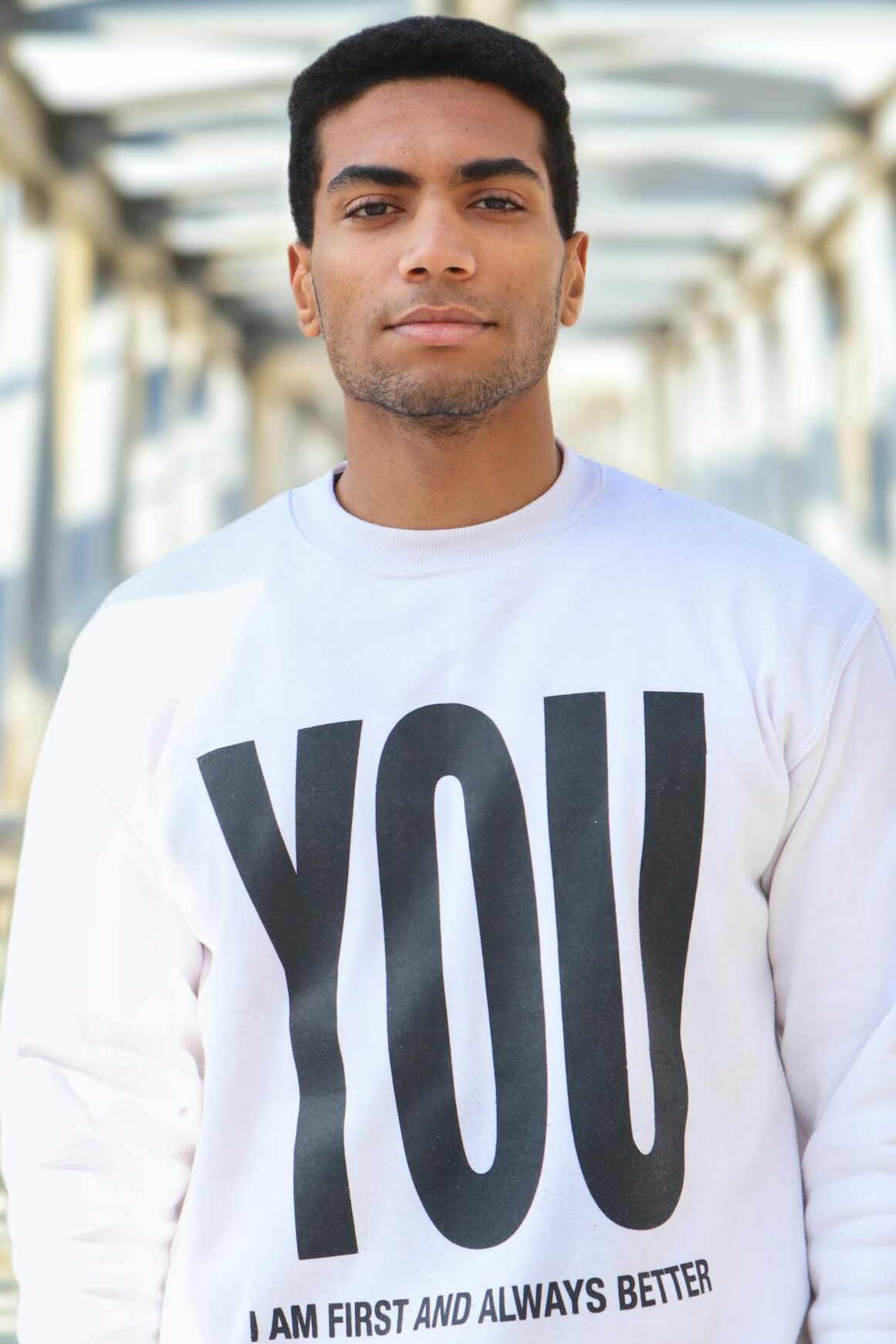 Portrait of a stylish man in a sweatshirt standing on a modern bridge.